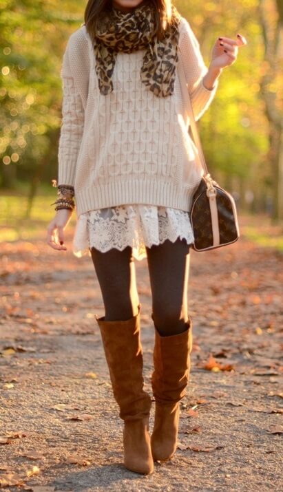 Woman in the park wearing a white lace dress, beige woolen sweater, brown leggings, leopard-print scarf and brown boots