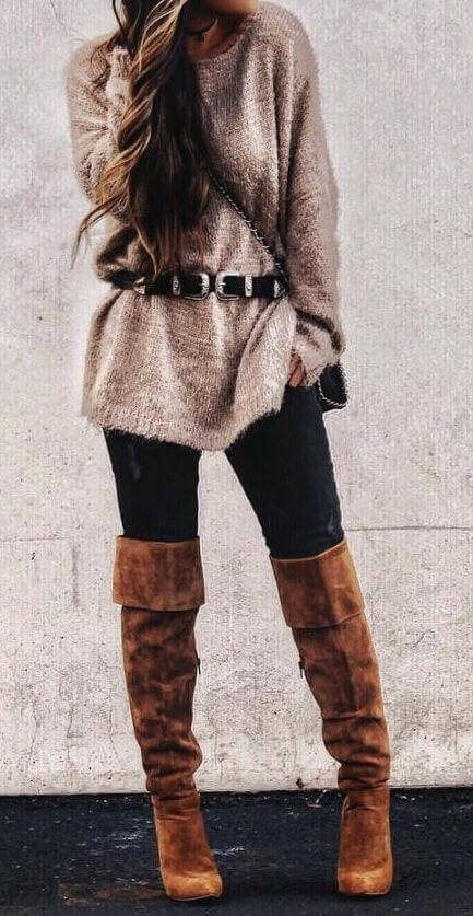 Woman wearing distressed black jeans, a beige oversized wool sweater, black buckle belt and brown boots