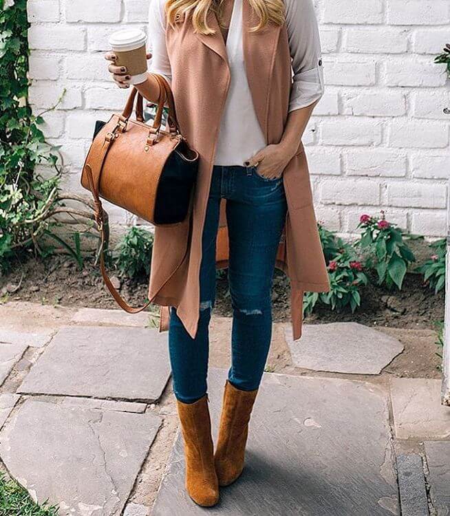 Woman wearing ripped blue jeans, white top, pink sleeveless duster jacket, brown leather handbag and brown boots
