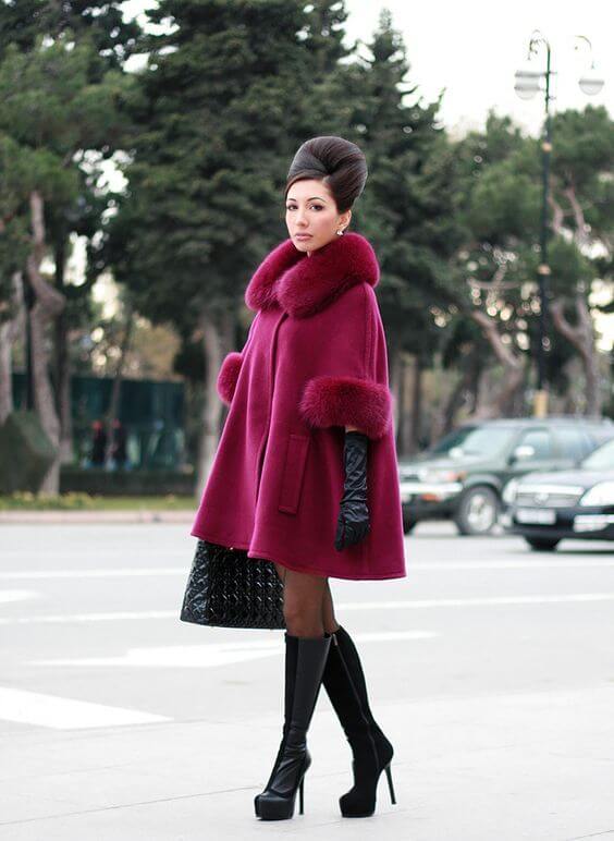 Woman wearing an oxblood swing coat, black knee length boots, and black gloves