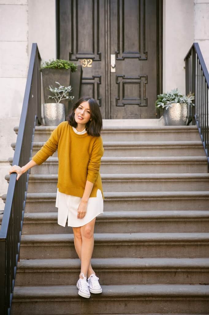 A girl dressed in a white shirtdress and mustard sweater