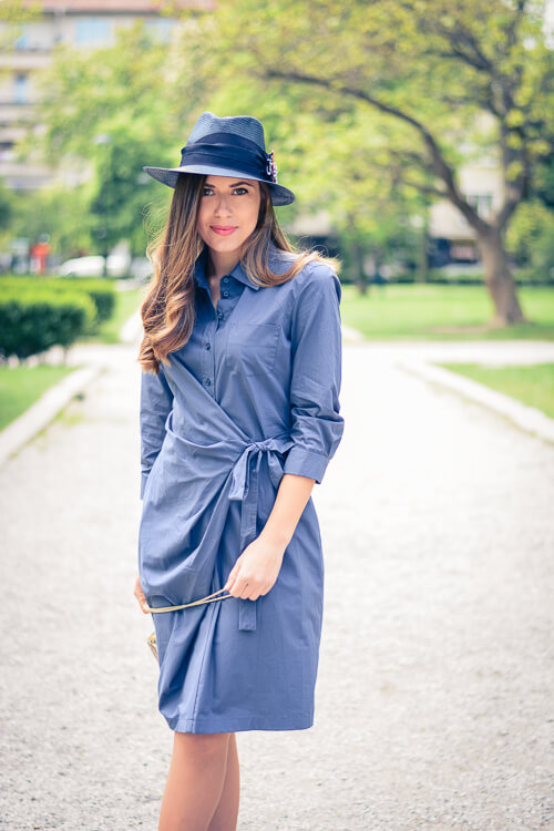 A woman walking in the park dressed in a solid blue dress with a wrap-over silhouette