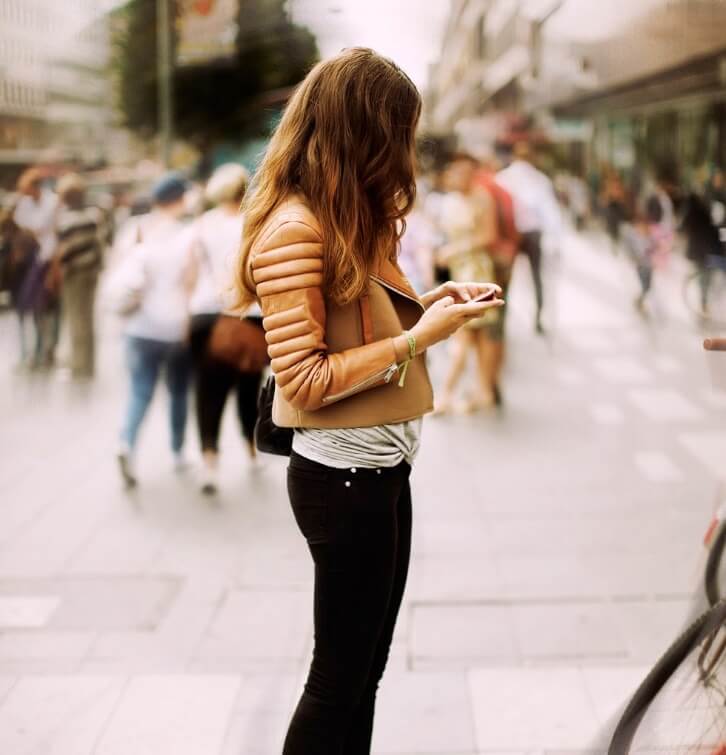 Woman on the street wearing black skinny jeans, light gray top and brown leather jacket