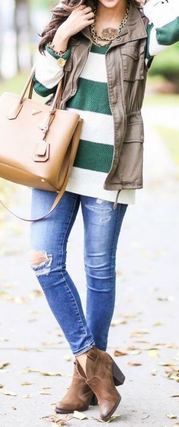 Woman wearing ripped blue skinny jeans, striped sweater, sleeveless khaki parka and brown boots