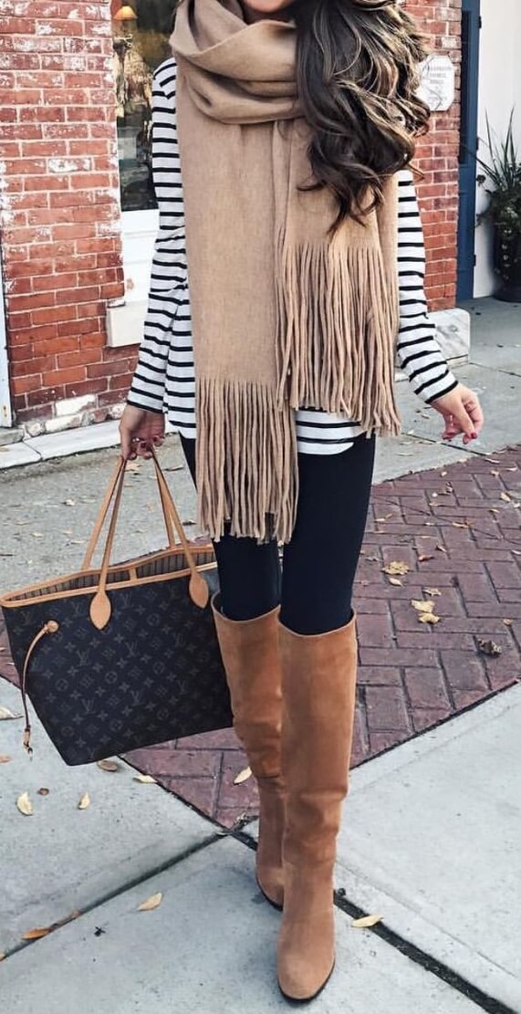 Woman on the street wearing black leggings, striped top, beige scarf, Louis Vuitton handbag and brown boots