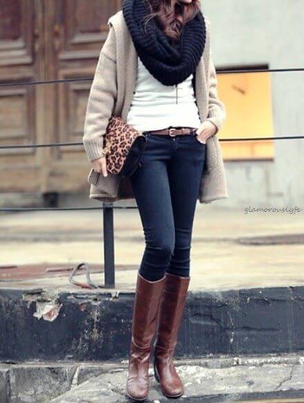 Woman wearing dark blue skinny jeans, white top, beige jacket, navy blue scarf and brown boots with a leopard-print envelope purse