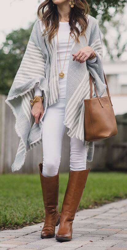 Woman wearing white jeans, white top, gray and white poncho, brown leather handbag and brown boots