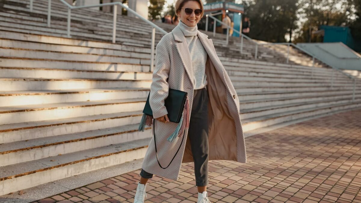 stylish confident fashionable woman walking in street in elegant style coat wearing sunglasses, bag and white boots, business lady style, winter autumn spring style fashion