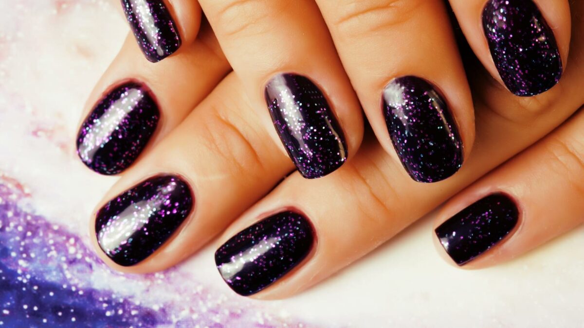Woman fingers with nails purple glitter on nails like cosmos, universe background