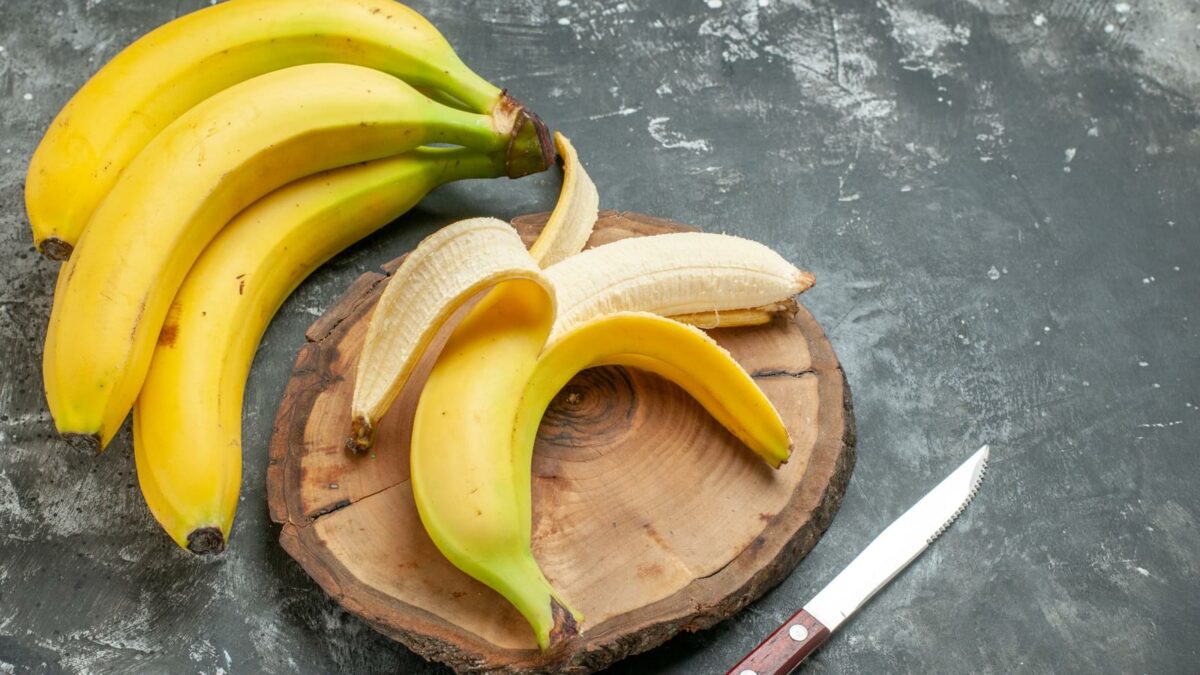 Top view nutrition source fresh bananas bundle and peeled on wooden cutting board knife on gray background
