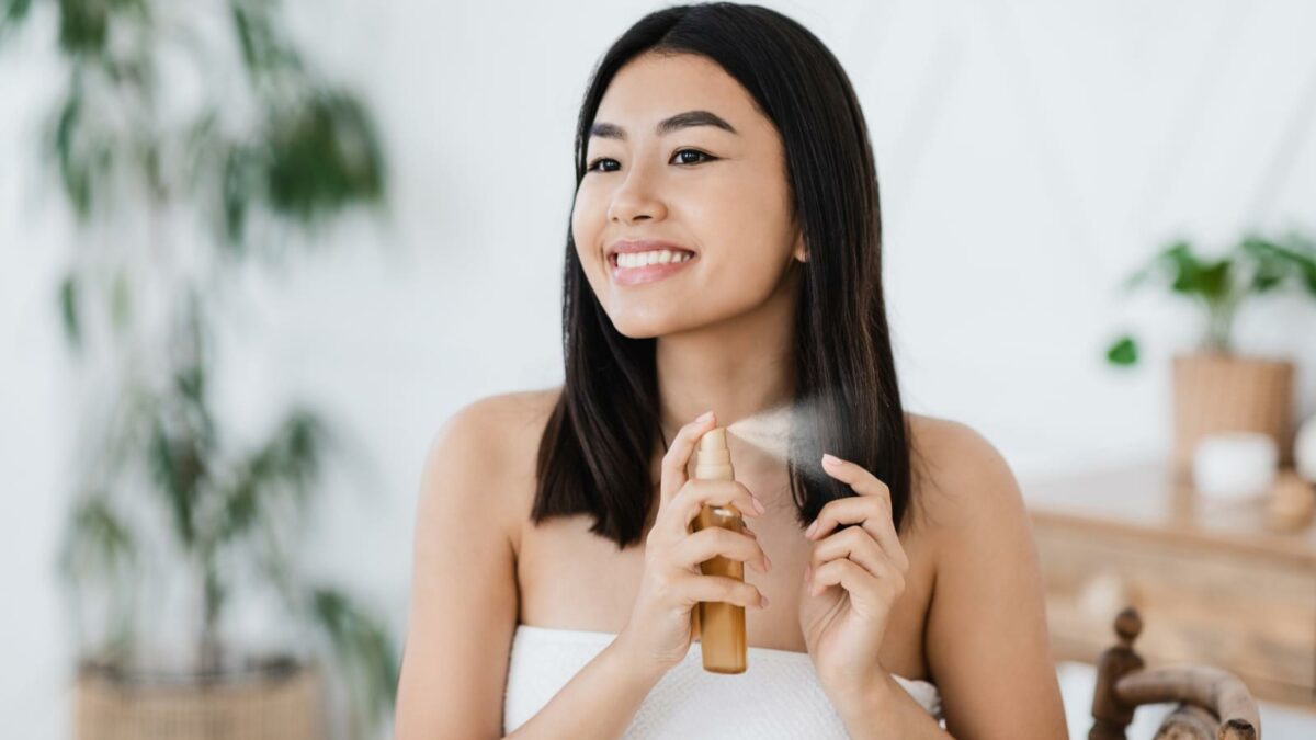 Pretty happy asian girl applying hair oil to prevent split ends, hair care at home concept, copy space