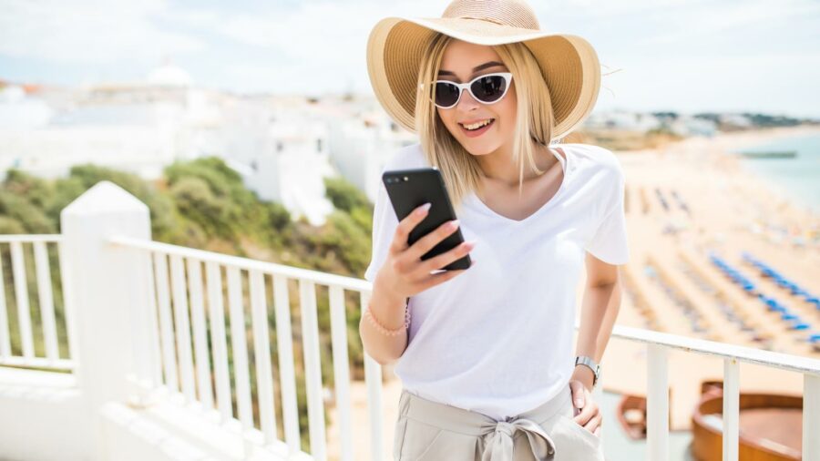Attractive young woman typing on phone on terrace on beach view background.