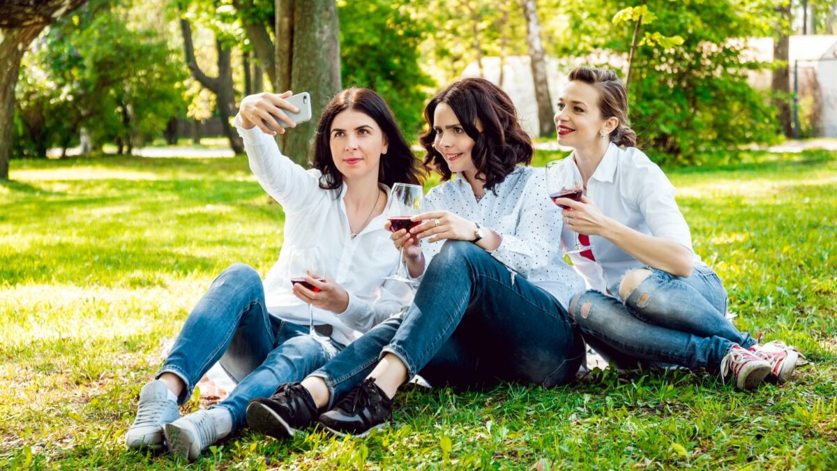 Young beautiful girls with glass of red wine in the park. Nature background