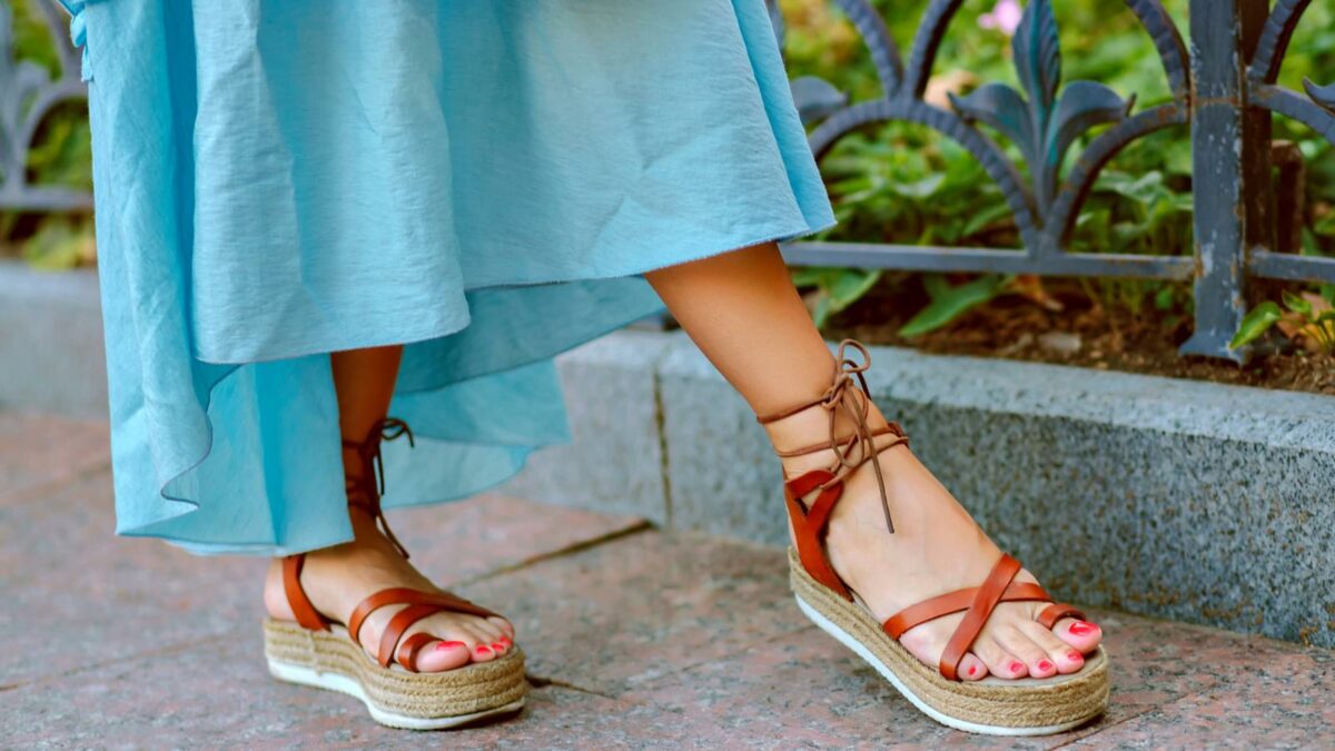 Close up fashion details of woman feet’s, elegant gladiator sandals, blue feminine dress, perfect for summer vacation.
