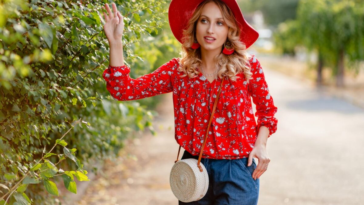 Pretty attractive stylish blond smiling woman in straw red hat and blouse summer fashion outfit in park boho style