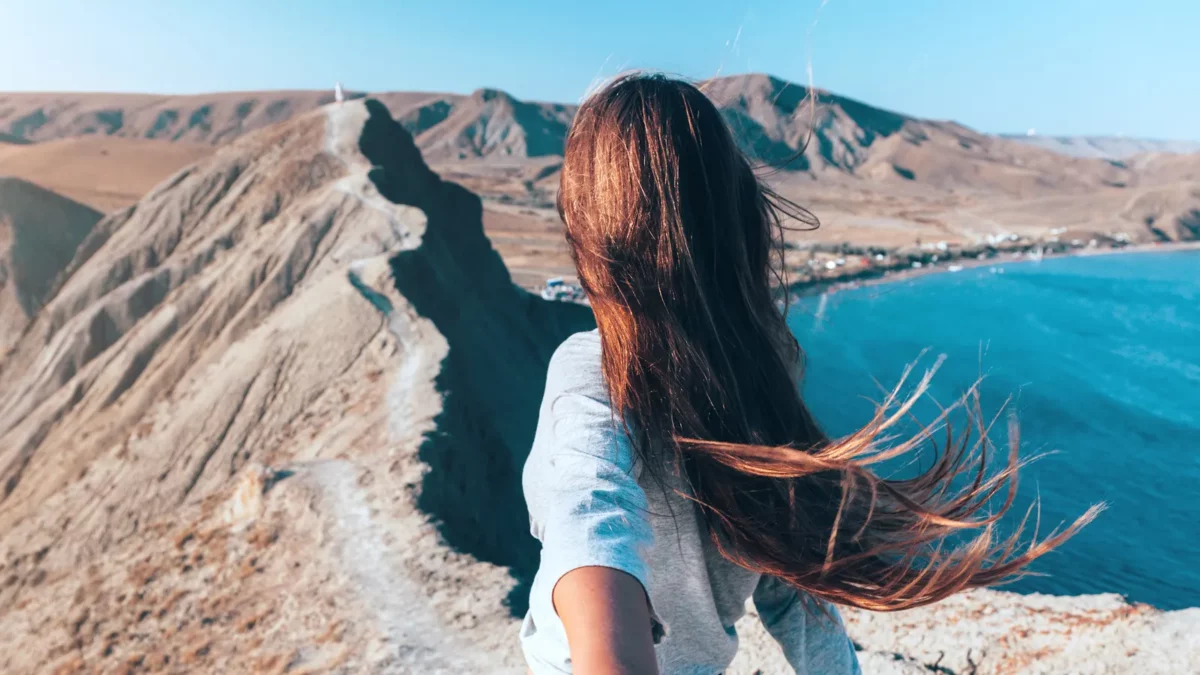 Girl walking on the mountain top over blue sea