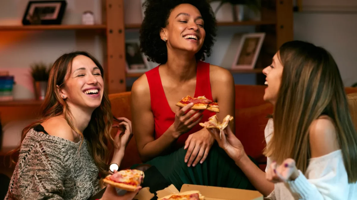 A multicultural group of cheerful young women is eating pizza