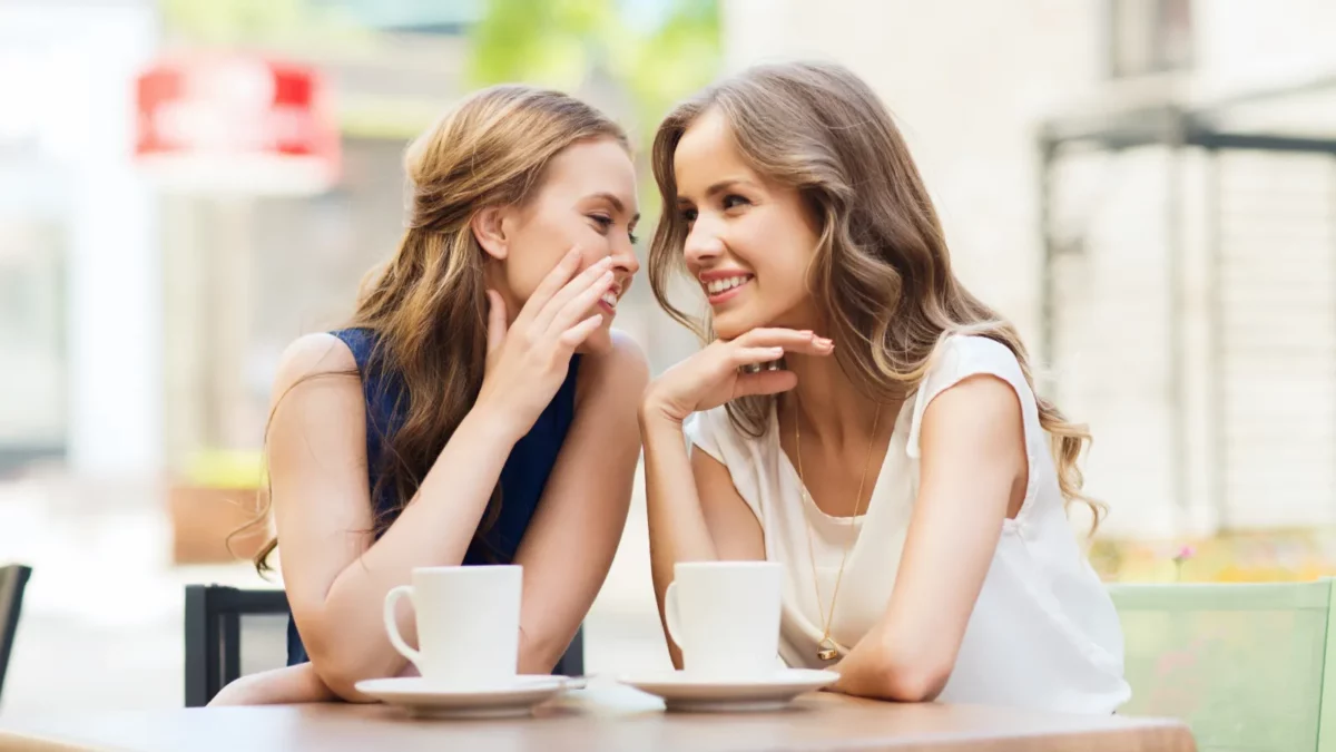 Smiling young women drinking tea and gossiping at outdoor cafe