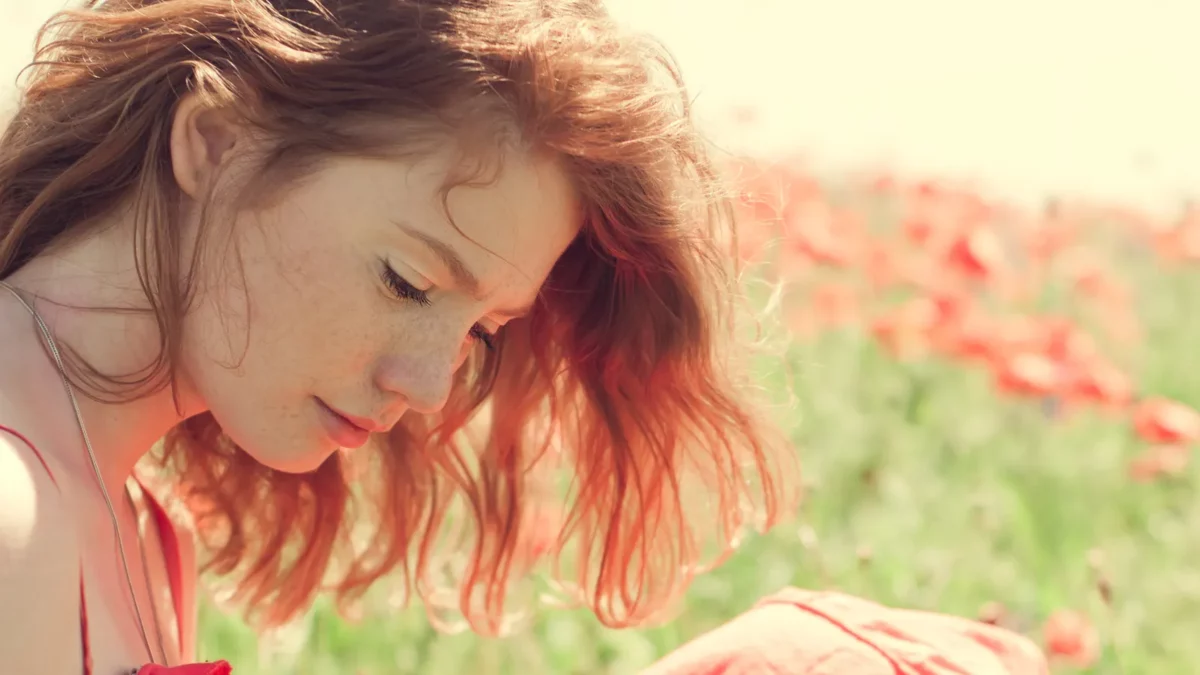 Red haired girl with freckles in a summer field