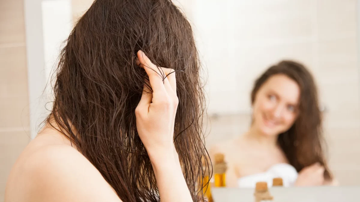 Smiling young woman applying oil mask to her hair