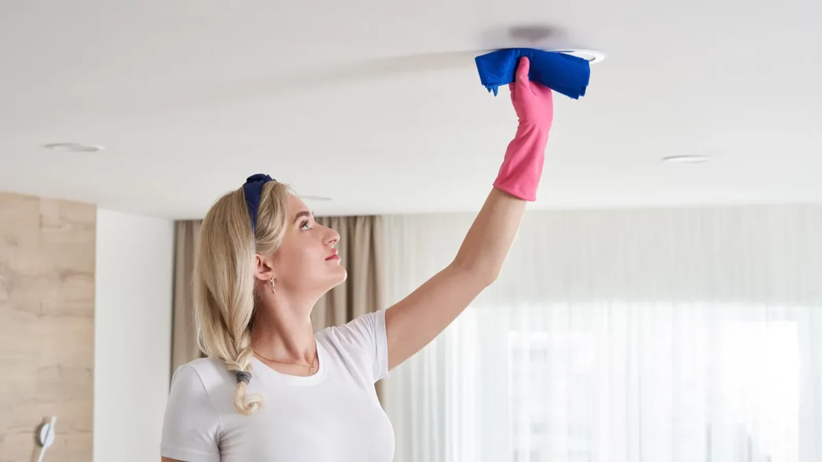Woman cleaning ceiling in living room