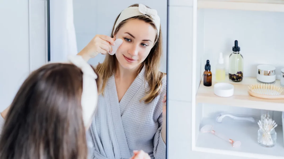 Woman in bathrobe making face massage with gua sha roller