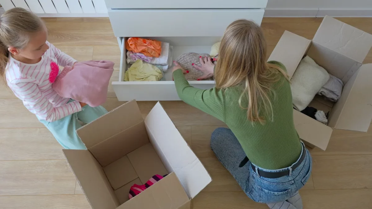 Little girl with mother putting clothes to drawer