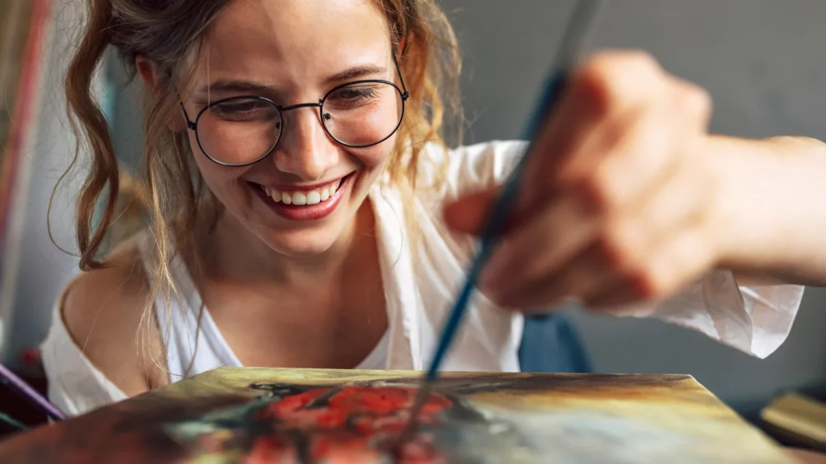 Smiling artist painting with a brush on canvas